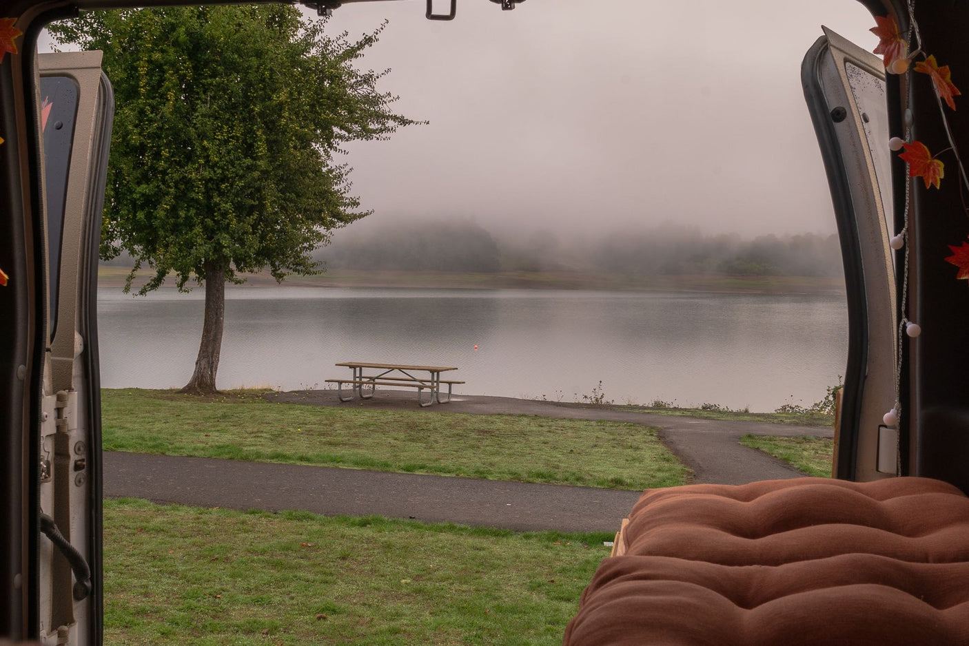 Misty lake view from an RV rental, featuring a tree, picnic table, and scenic path. A cozy campervan retreat.
