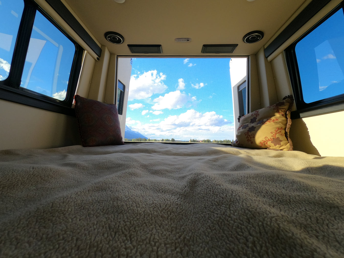 Relax in your RV rental with a panoramic view of blue skies, clouds, and mountains from the comfort of your bed.