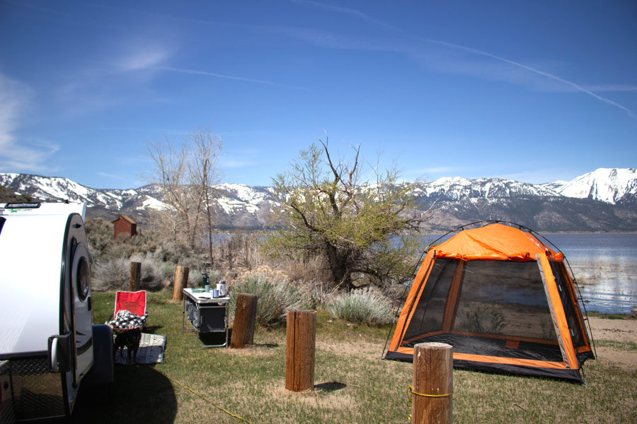 Lakeside campsite with a white RV rental, orange tent, and snow-capped mountains. Ideal for scenic nature camping.