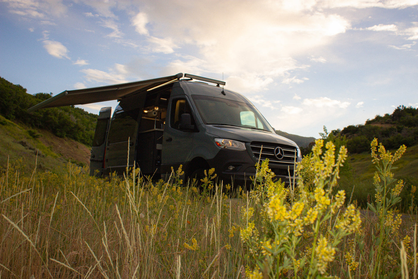 Adventure awaits! Dark gray Sprinter RV rental with awning extended, parked in a field of yellow flowers.