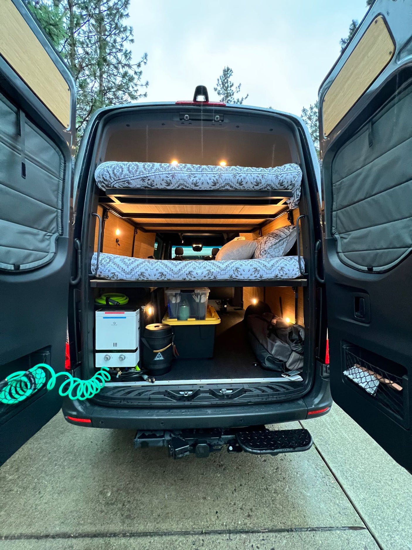 Inside an **RV rental** campervan, rear view: cozy bunk beds, portable water heater, and organized storage for mobile adventures.