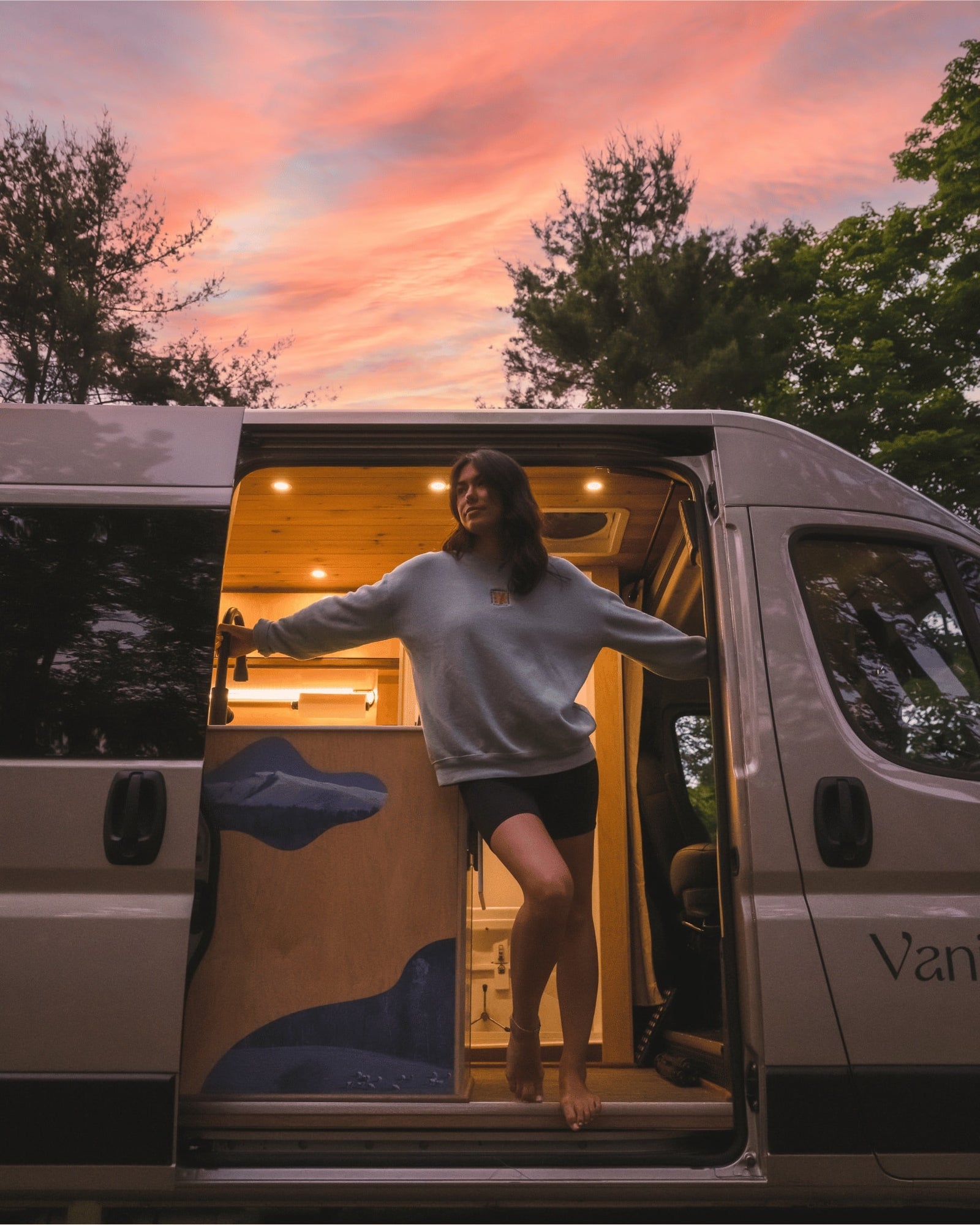 and compact wet bath for comfortable travel.|Cozy RV rental view: Person with blanket and mug enjoying autumn nature by the river from inside a campervan.|RV rental: See inside this custom camper van's rear