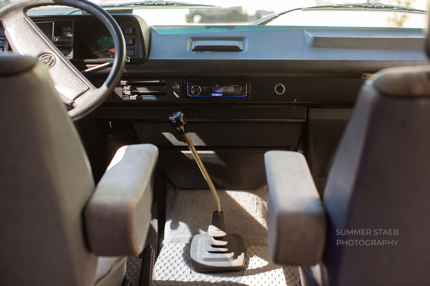 Interior of an RV rental: dashboard, steering wheel, and manual gear shift in a classic VW van.