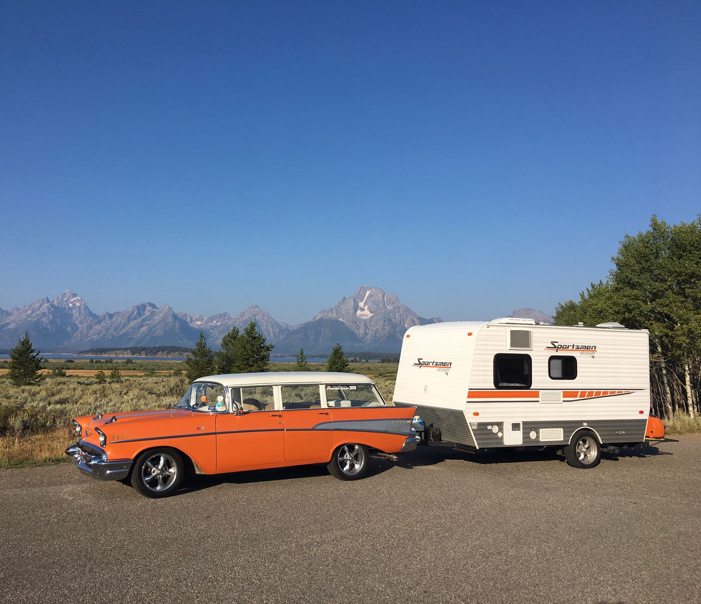 Orange vintage car & Sportsmen RV rental parked with Grand Teton mountains & lake. Classic road trip!|This white Sportsmen Classic travel trailer