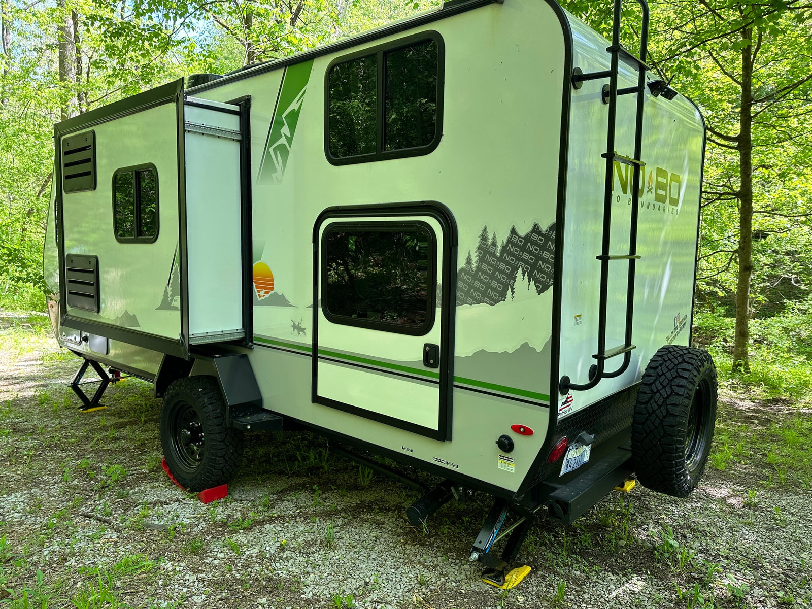 This sleek NO BO travel trailer, featuring an expandable side and off-road tires, is an ideal RV rental for exploring wooded campsites.