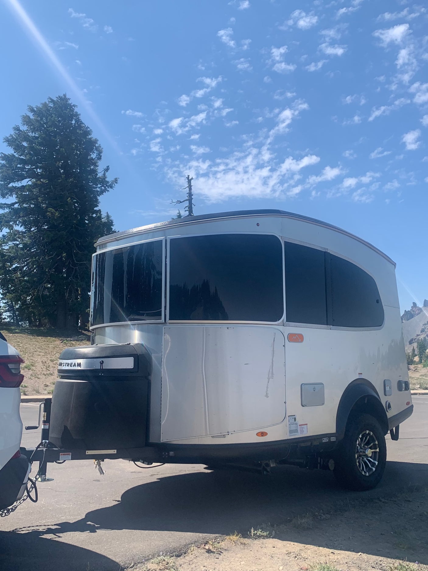 This Airstream Basecamp RV trailer, ideal for an rv rental adventure, shines under a sunny sky with trees and mountains.