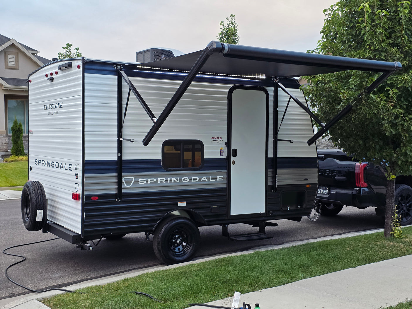 This new Springdale travel trailer, an RV rental, is parked with its illuminated awning extended, hitched to a pickup truck.