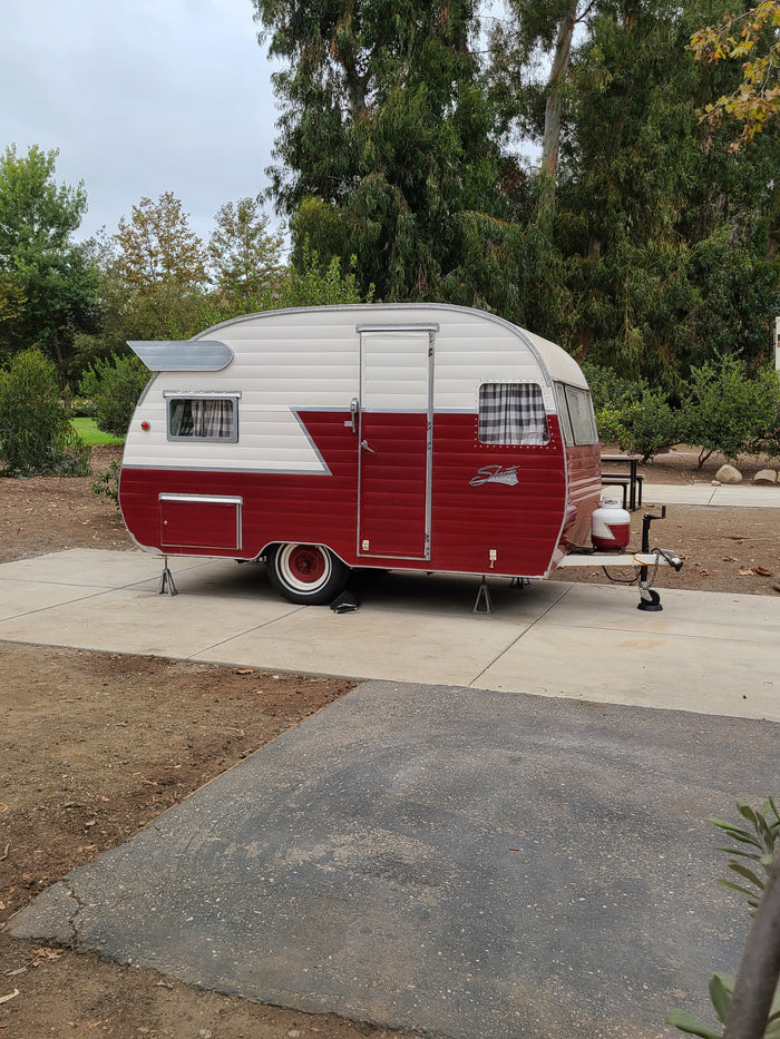 Retro red & white Shasta travel trailer, parked at a campsite, ready for your next RV rental adventure.