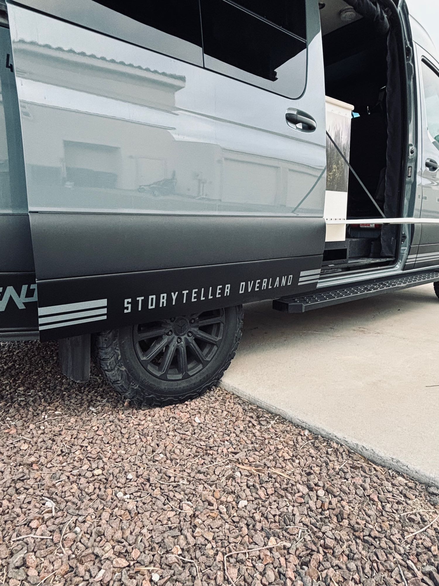 Gray Storyteller Overland van, open door showing interior, with off-road tires. Great RV rental for adventure.
