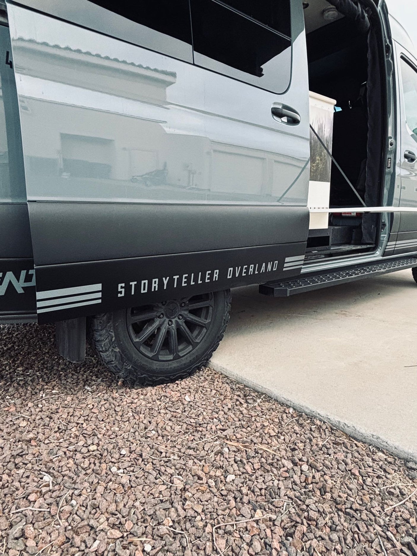 Gray Storyteller Overland van, open door showing interior, with off-road tires. Great RV rental for adventure.