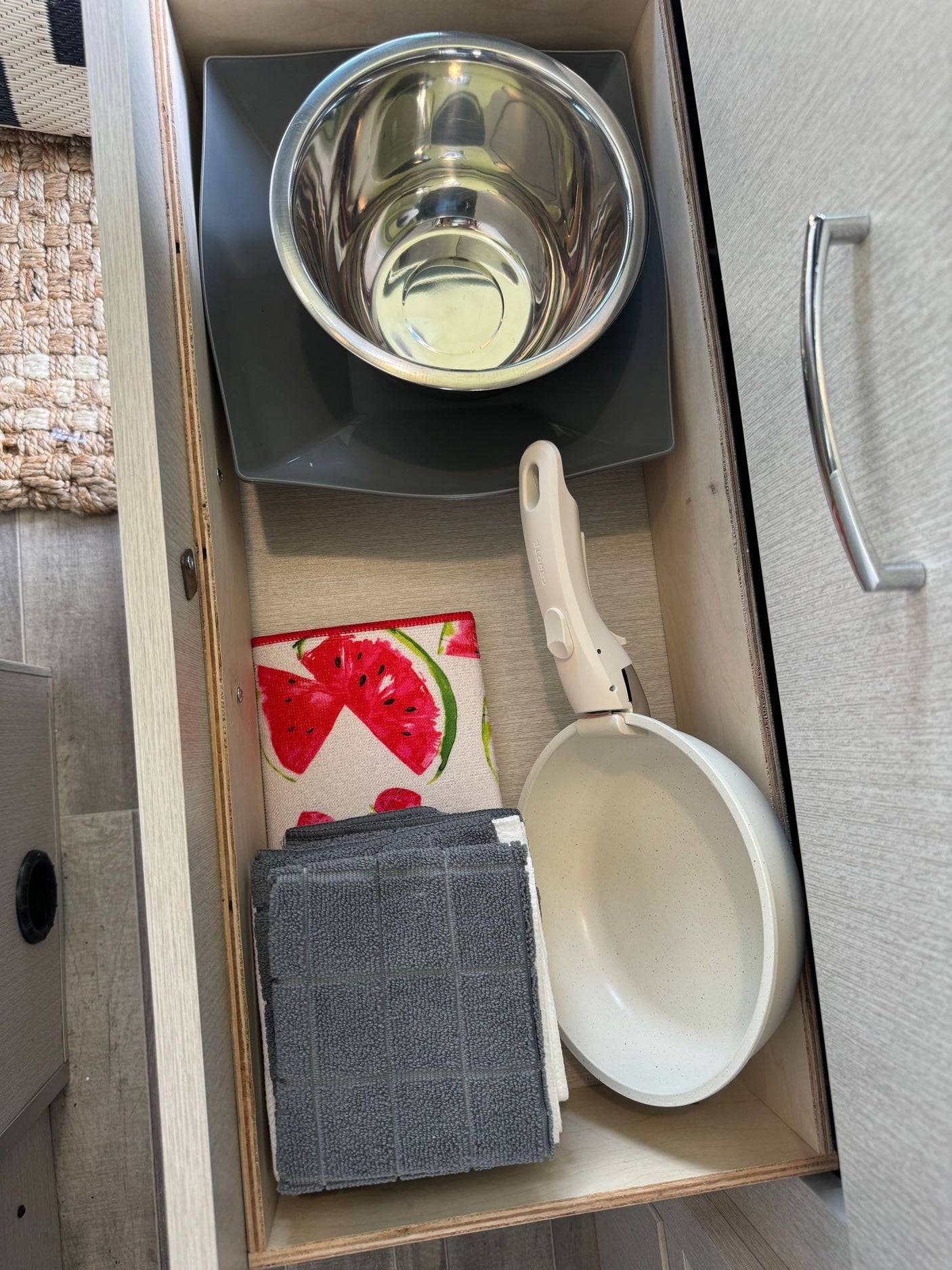 RV rental kitchen drawer: a mixing bowl, plate, pan with a detachable handle, and kitchen towels, neatly stored.