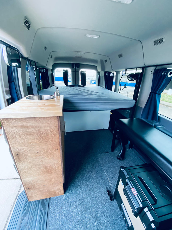 and seating.|Experience RV rental comfort: a cozy bunk bed with blue privacy curtains