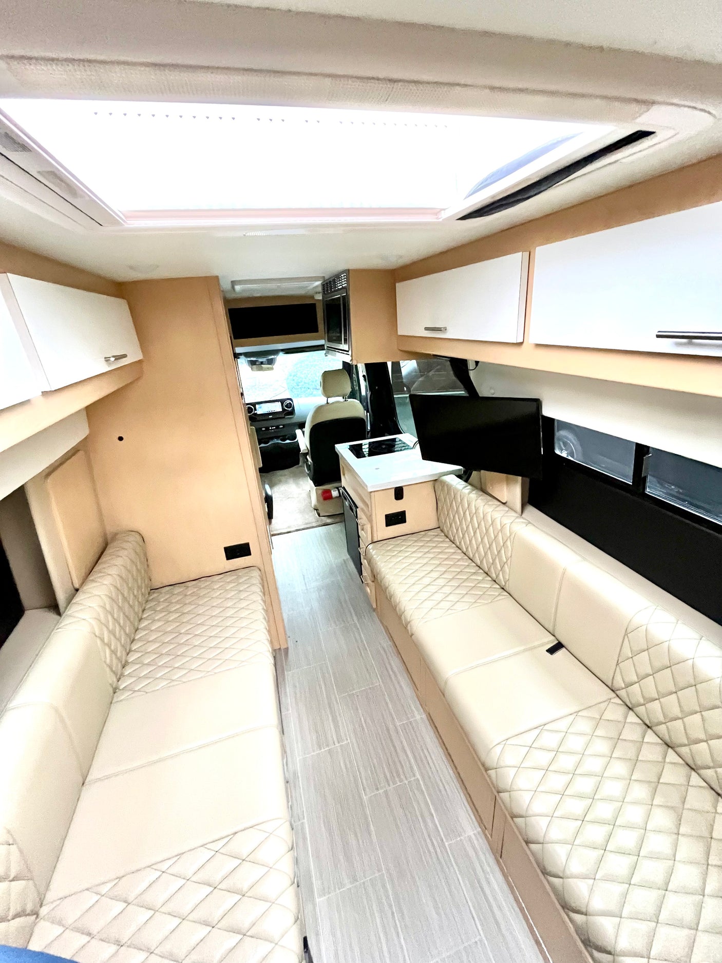Spacious RV interior with light quilted leather seating, central aisle, and kitchen area looking towards the driver's cabin, perfect for an rv rental.