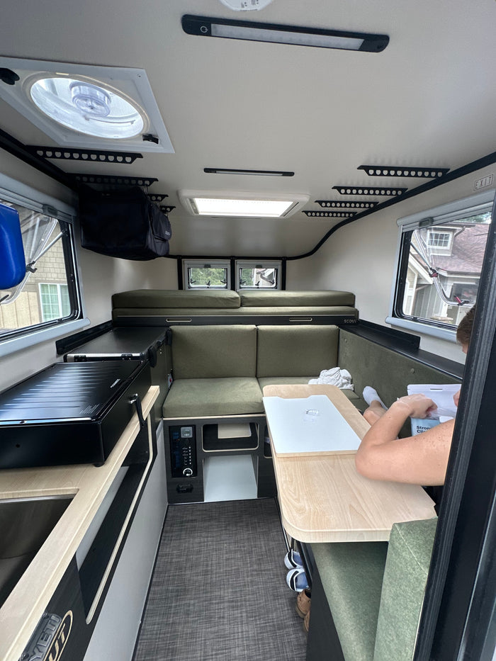 Experience compact living in this modern RV rental interior with a kitchenette, dining, and sleeping areas, perfect for adventure.