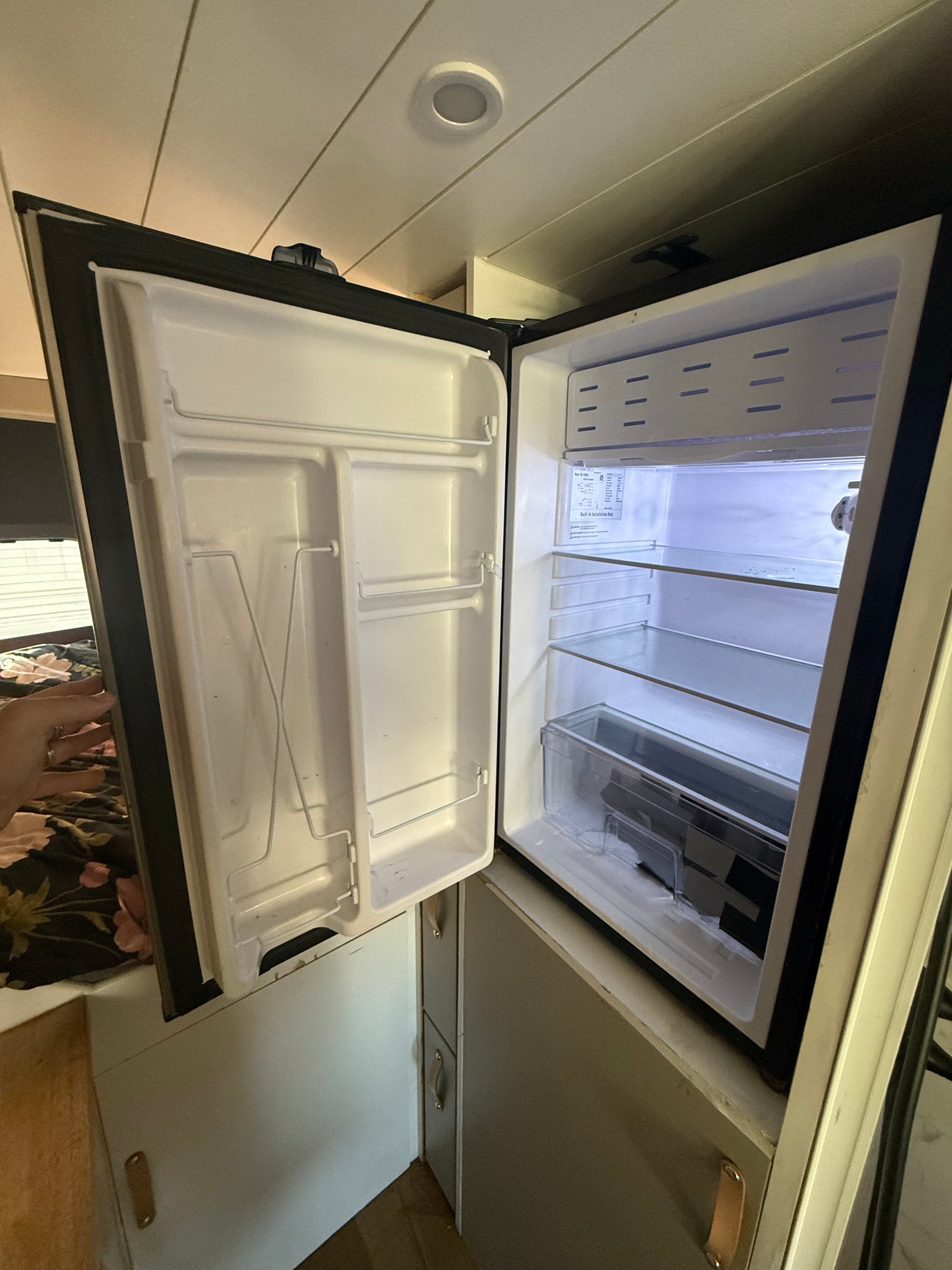 This image shows a clean, empty mini-fridge inside an RV rental, featuring shelves and a crisper drawer, ready for use.