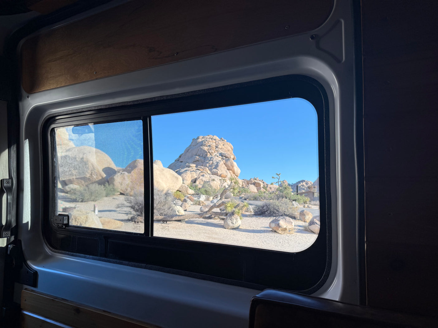 Inside an RV rental: a window view of stunning desert rock formations under a bright blue sky.