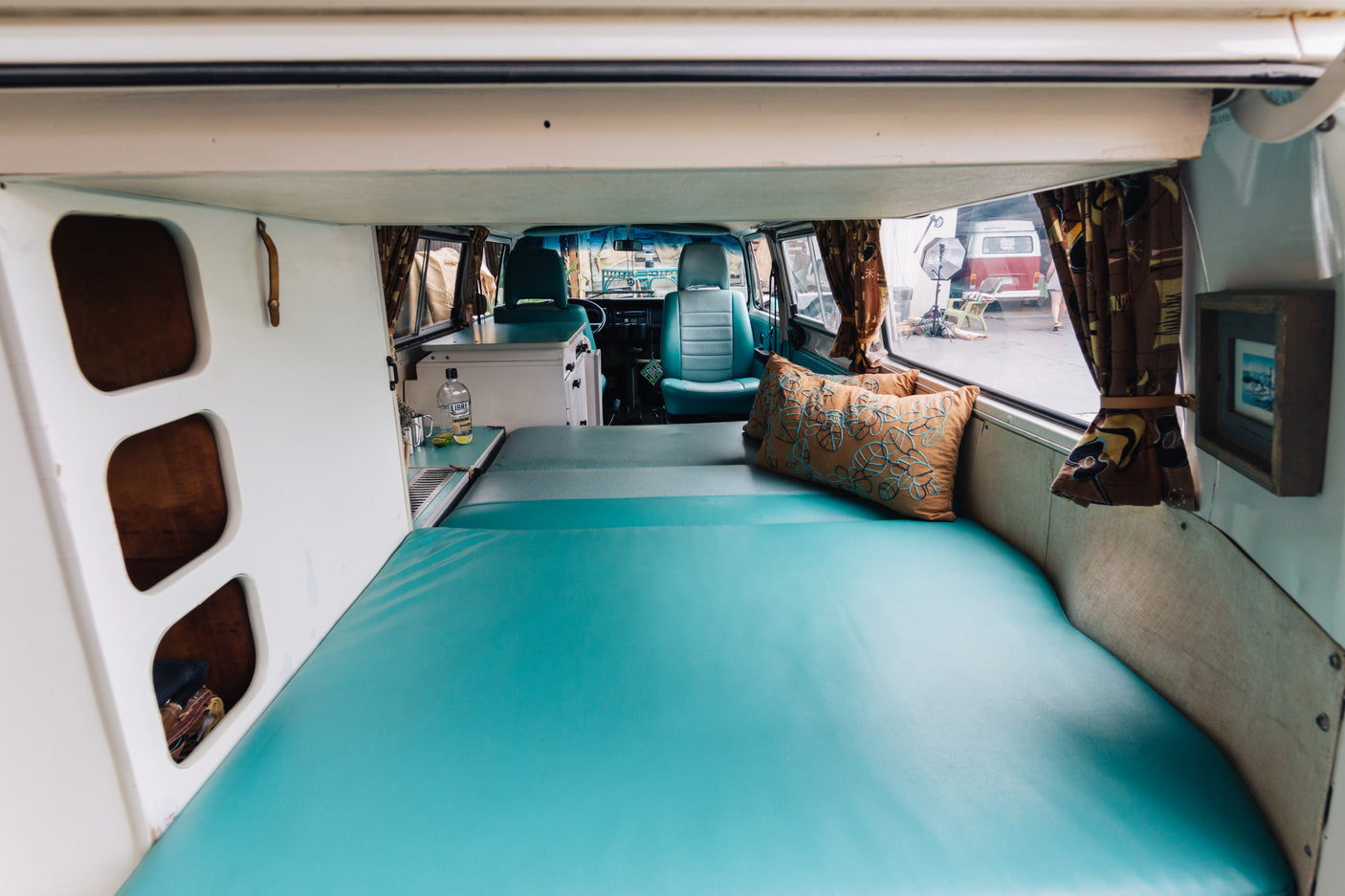 Inside a bright custom RV rental with a wide teal bed, compact kitchen, and inviting front cabin. Ideal for road trips!