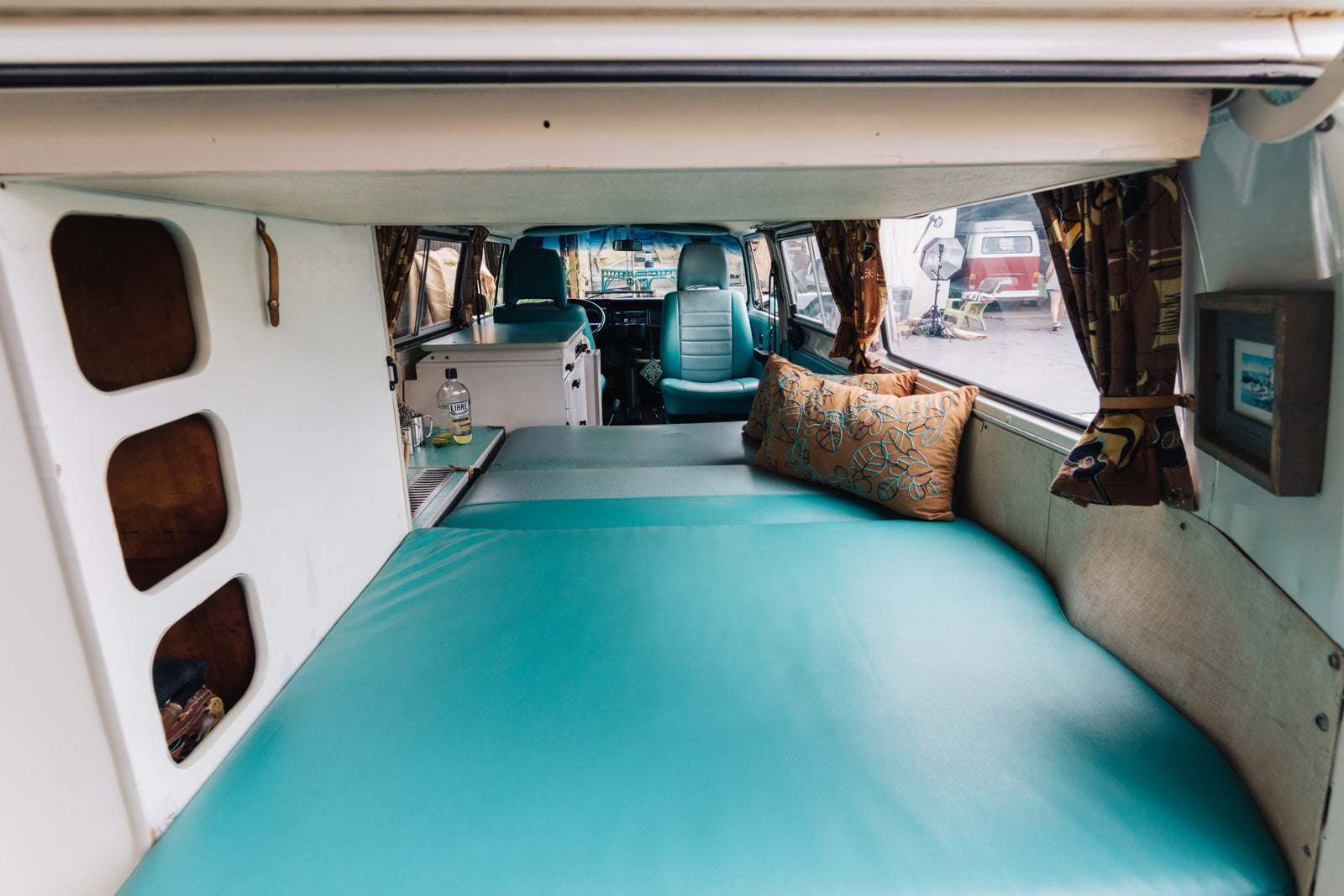 Inside a bright custom RV rental with a wide teal bed, compact kitchen, and inviting front cabin. Ideal for road trips!