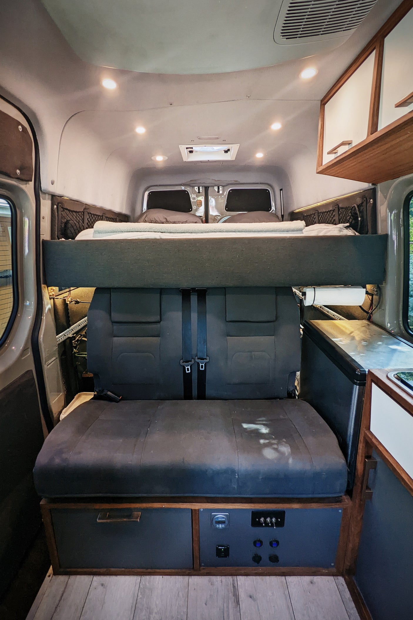 RV rental interior: elevated bed over rear seats, kitchen, and power control panel. Ready for your camper van trip.