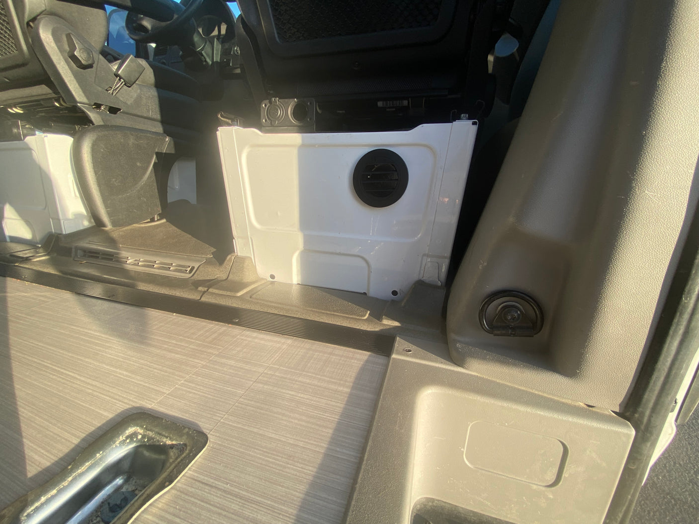 RV rental interior: white utility box with vent, faux wood floor, and seat base.