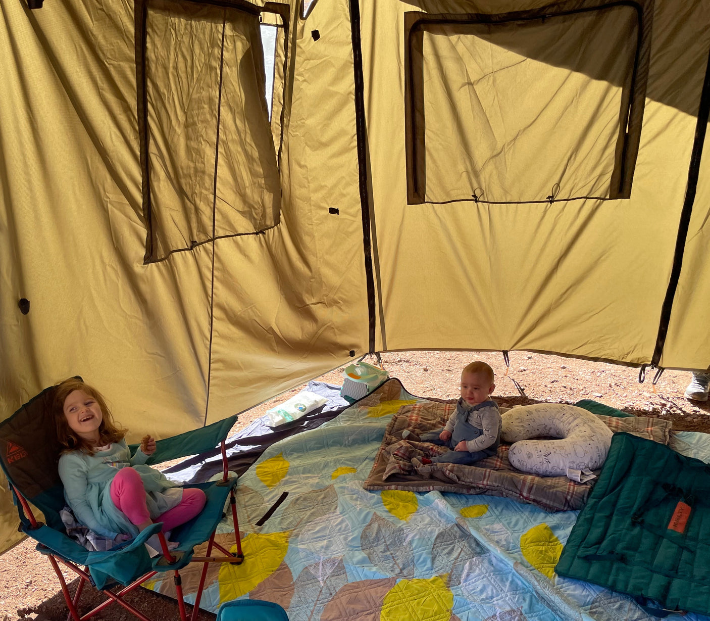 Inside a spacious RV rental tent, a girl and a baby relax on blankets. Cozy family camping fun!