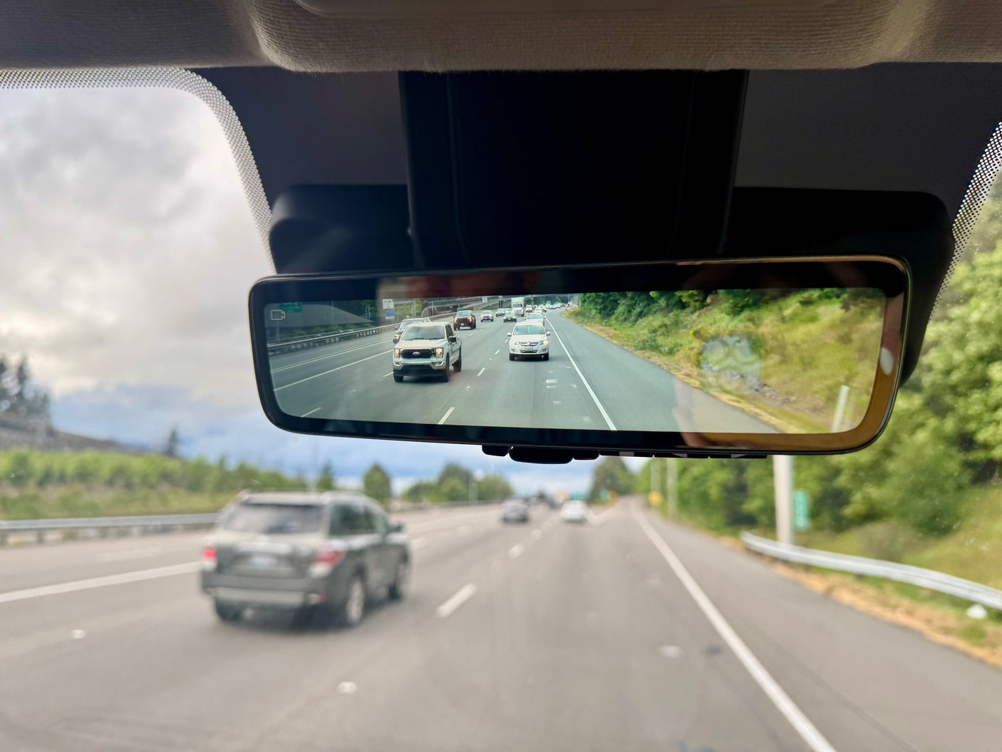 View from an RV rental's digital rearview mirror showing highway traffic, including a white truck, with a blurred SUV upfront.