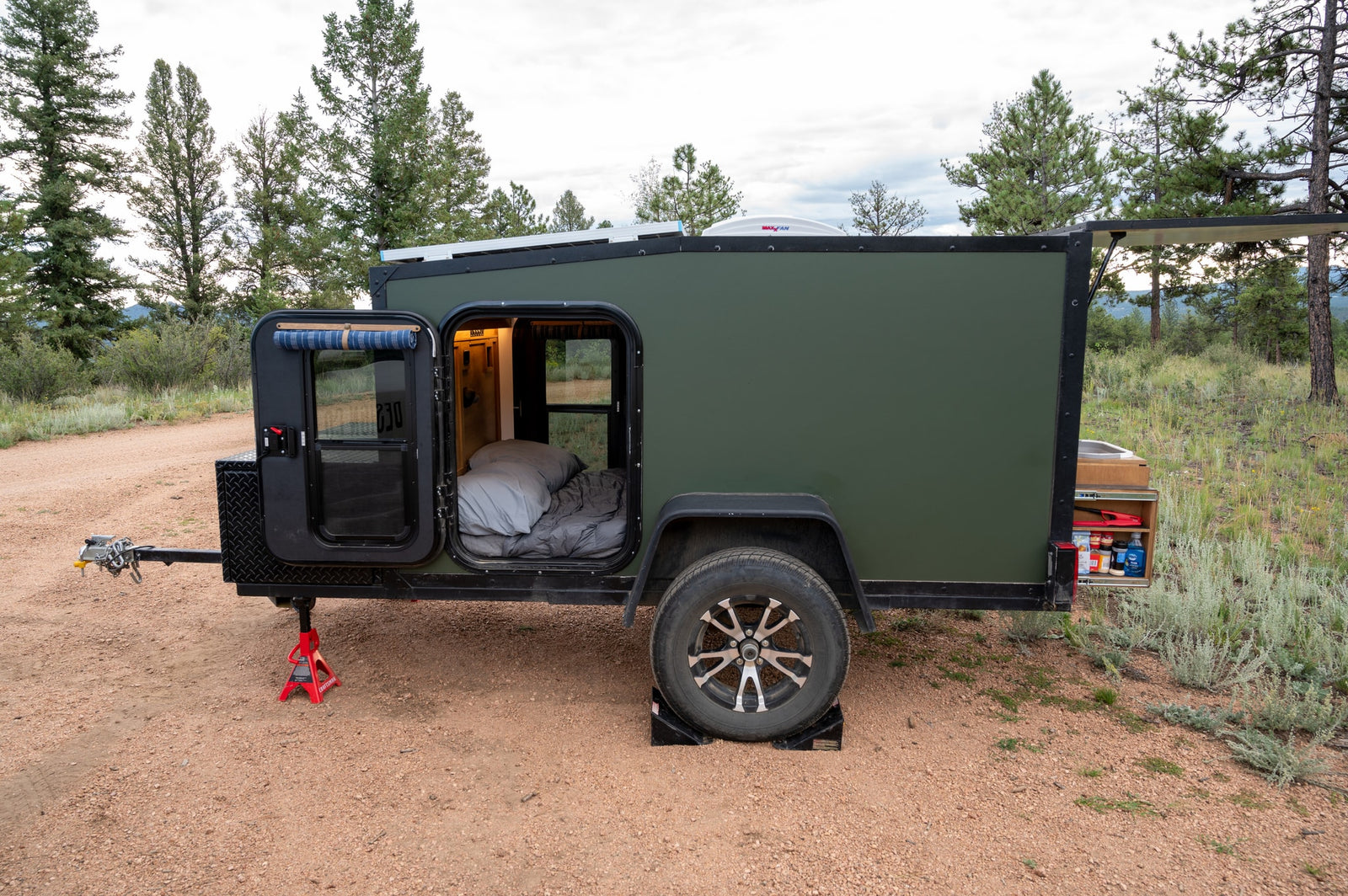 Compact green rv rental, a travel trailer, set up for camping. Doors open reveal a bed; rear galley shows stored items. Perfect for outdoor adventures.