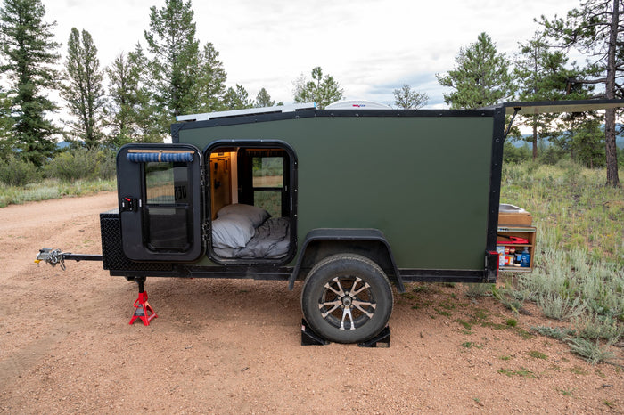 Compact green rv rental, a travel trailer, set up for camping. Doors open reveal a bed; rear galley shows stored items. Perfect for outdoor adventures.