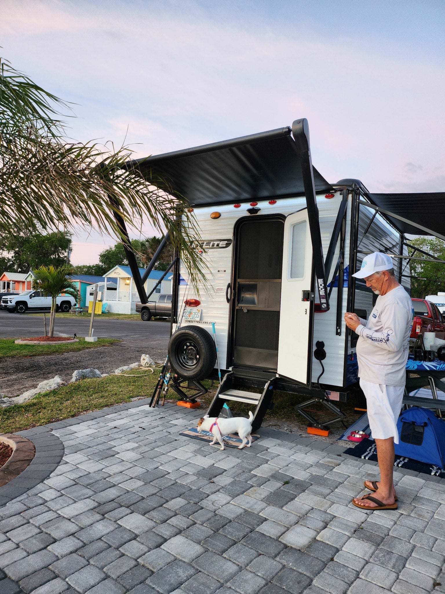 Evening at an RV rental site: Man with dog next to a white travel trailer