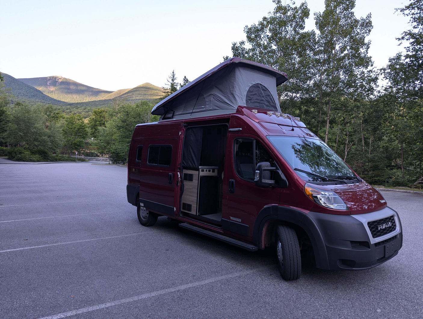 A red Winnebago Solis camper van rv rental with its pop-top extended, parked in a scenic mountain parking lot.