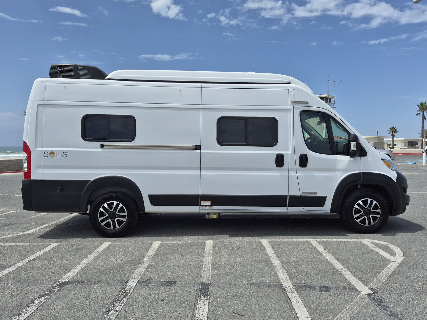 with palm trees and sand dunes visible. Florida plate 66F VUM.|White Winnebago Solis RV rental parked outdoors — photo 9