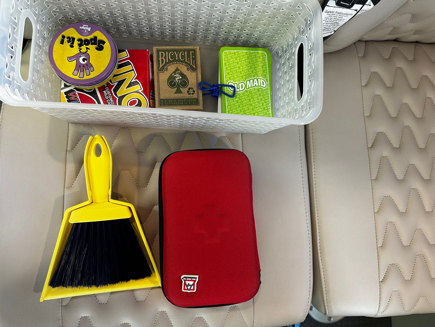 Organized RV rental: Basket of games (Spot It!, UNO, cards) for travel entertainment, with a handy dustpan and red case on the cream seats.