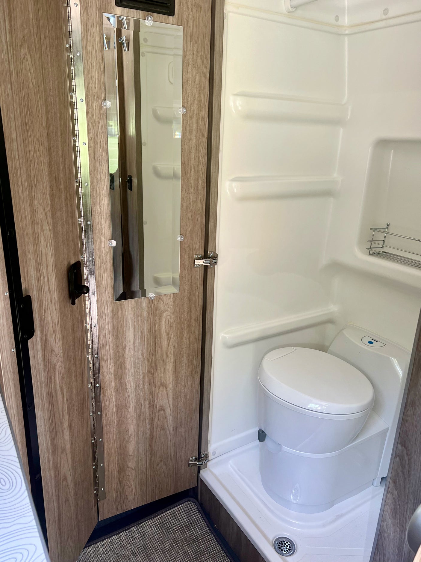 RV rental's compact wet bath features a toilet, shower, and mirrored door, maximizing space efficiency.