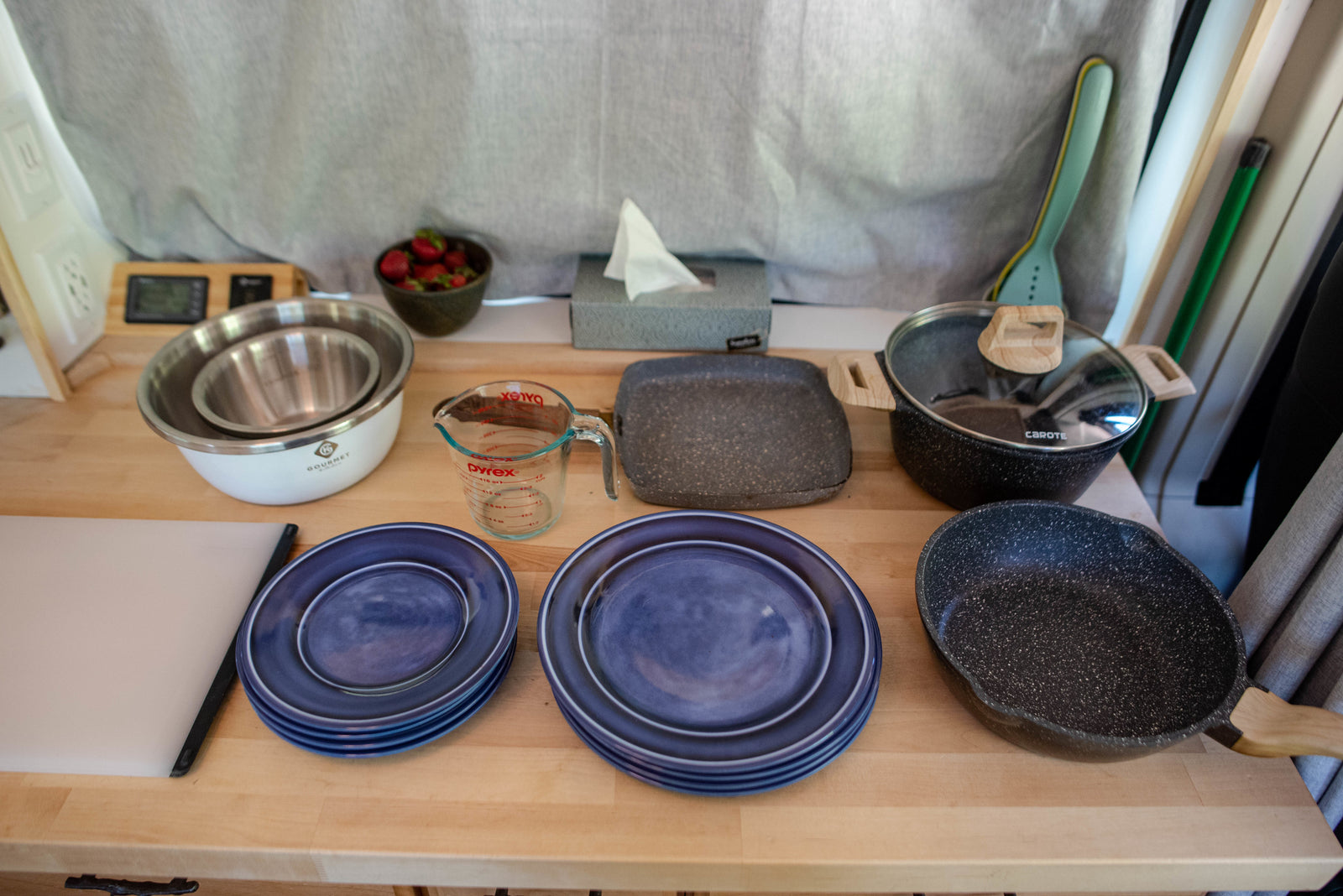 Inside an RV rental: a compact kitchen counter with blue plates, mixing bowls, Pyrex measuring cup, and speckled pots & pans.