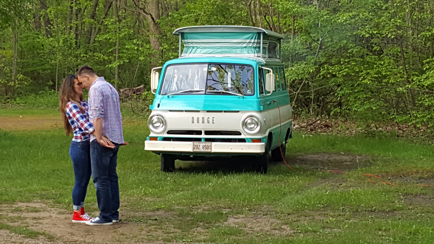 Embracing couple with a vintage turquoise & white Dodge camper van. Ideal RV rental for romantic adventures!