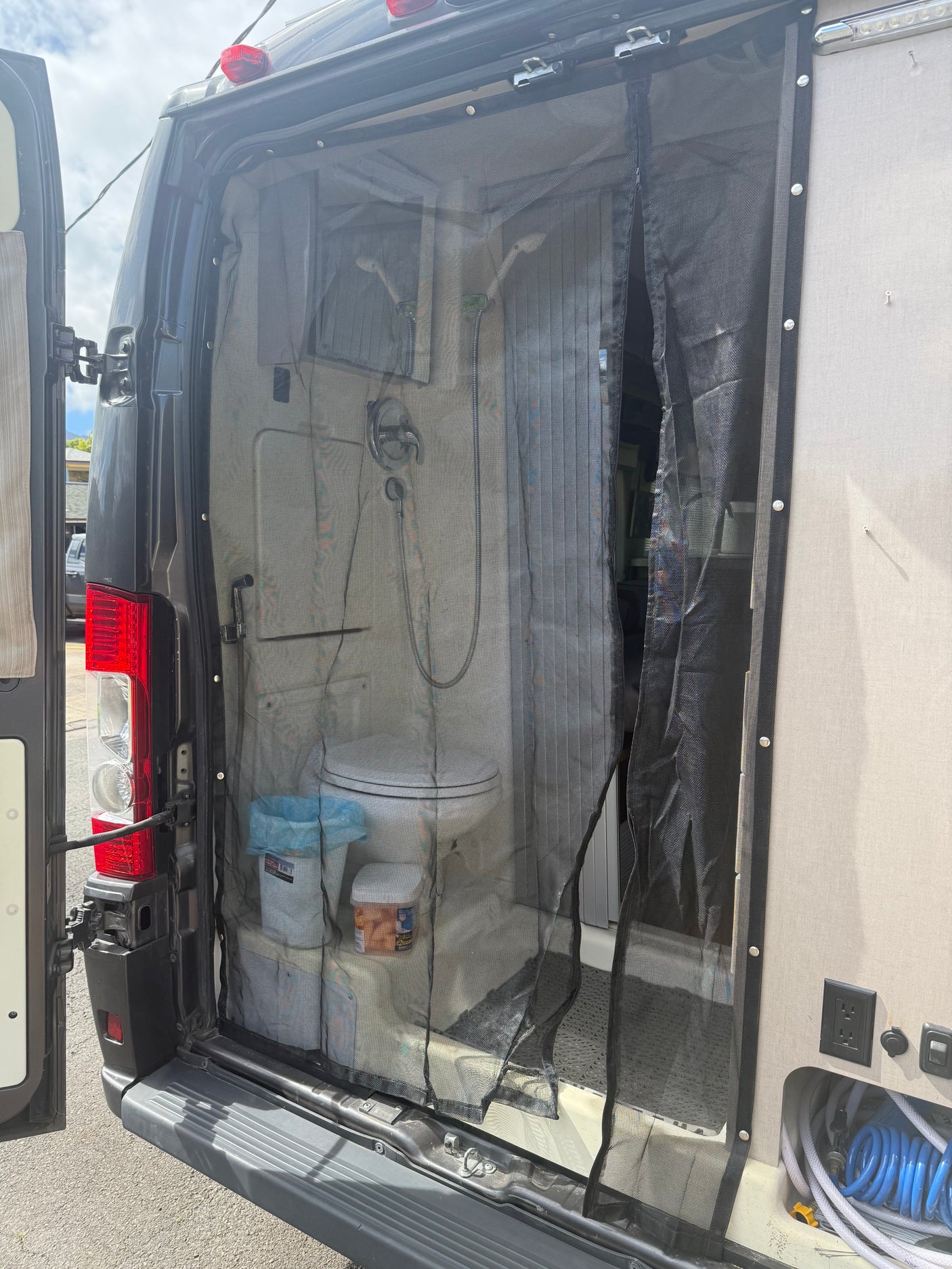 RV rental interior: Rear view of a campervan with mosquito net, toilet, and shower in a compact space.
