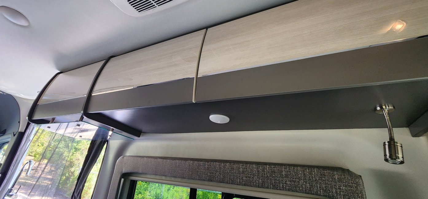 RV rental interior: modern overhead cabinets (light wood & dark grey), under-cabinet lights, and a flexible reading lamp.