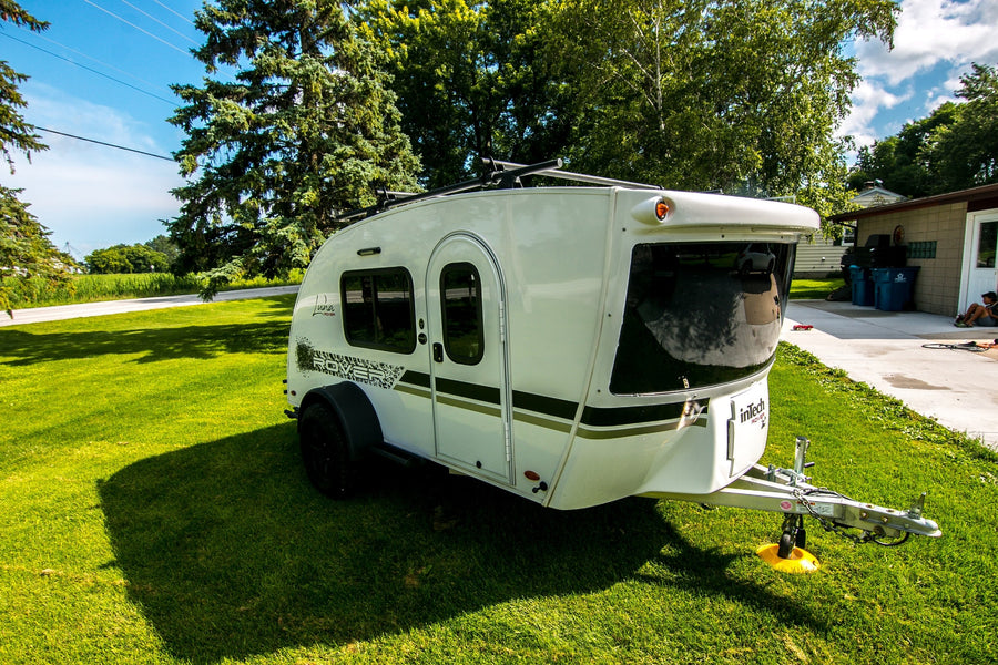 White inTech Luna Rover teardrop **RV rental** travel trailer, parked on vibrant green grass in front of trees.