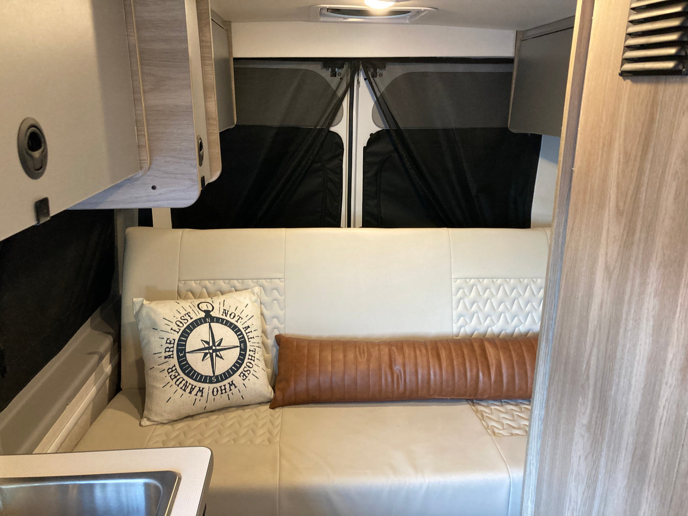Inside a comfortable rv rental, featuring light-colored seating with decorative pillows, cabinetry, and window covers.