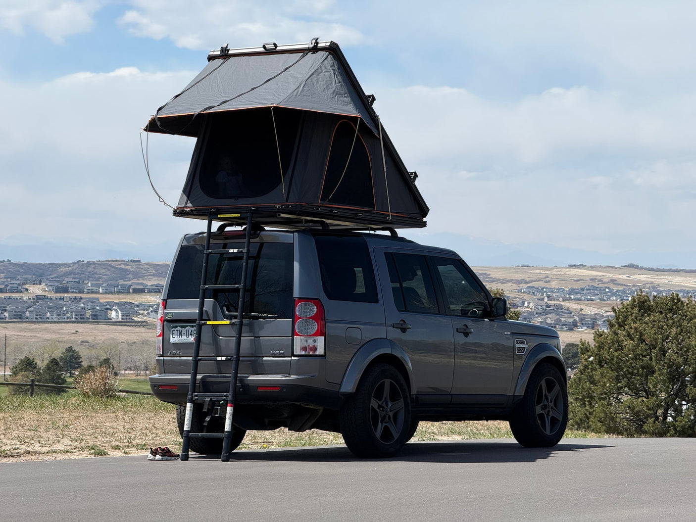 Dark gray Land Rover LR4 with a deployed rooftop tent, ready for an RV rental adventure in the scenic Colorado landscape.
