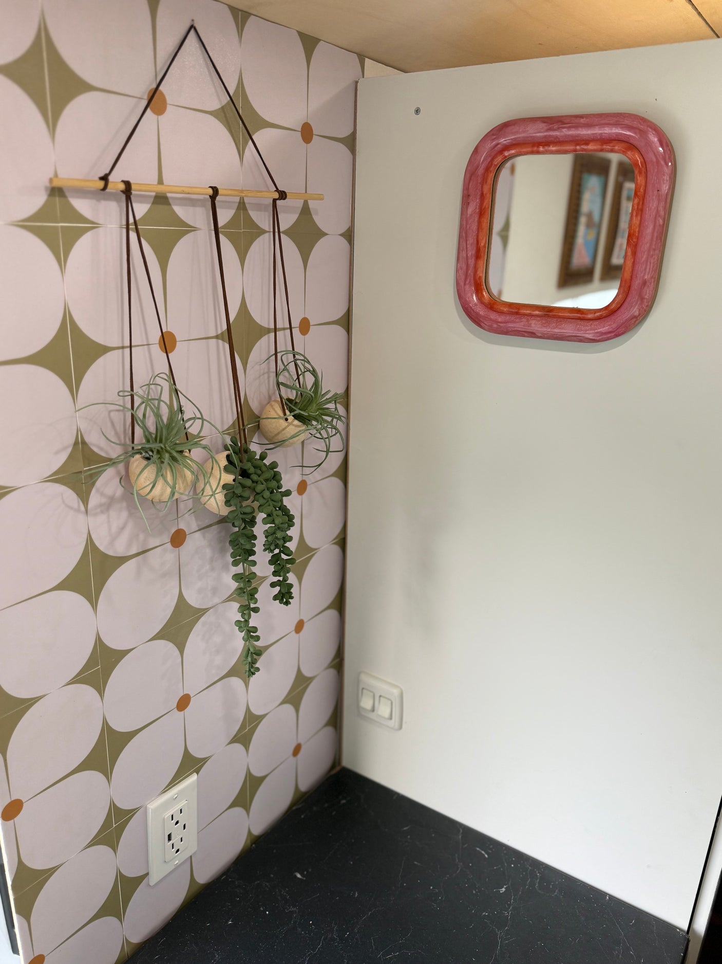 Inside an RV rental: Floral wall tiles, hanging plants, and a pink mirror create a cozy, decorated space with countertop & outlets.