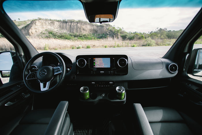 RV rental interior: Dashboard, nav screen (CA map), and green mugs. Road ahead visible for your next adventure.