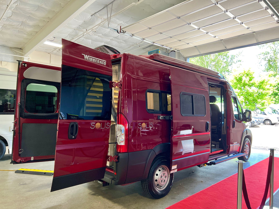 This red Winnebago Solis RV rental van is showcased on a red carpet with all doors open.