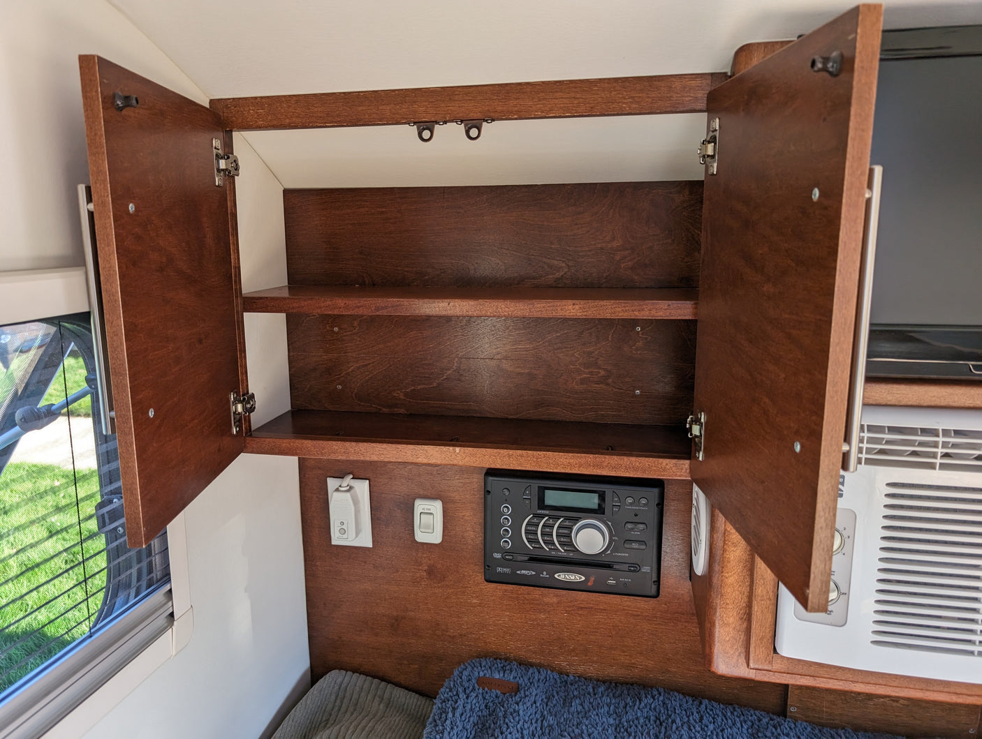 RV rental interior with open wooden cabinets showing shelves, a Jensen stereo, and AC controls for compact living.