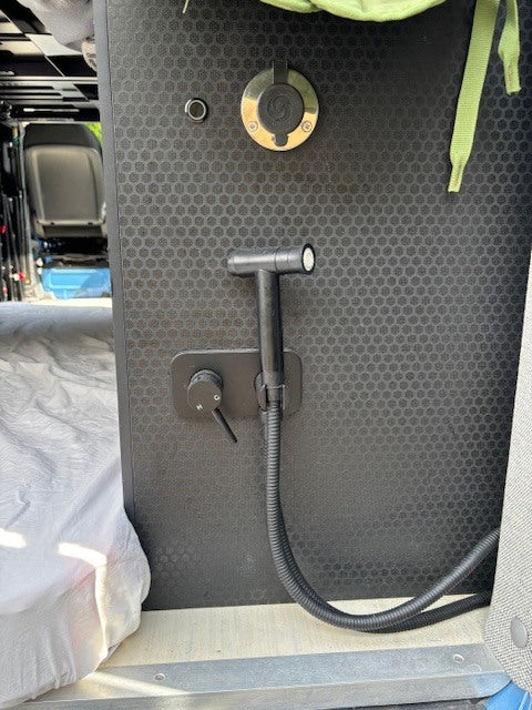 This RV rental van's flexible shower setup includes a quick-connect port, handheld head, hose, and water controls on a black panel.