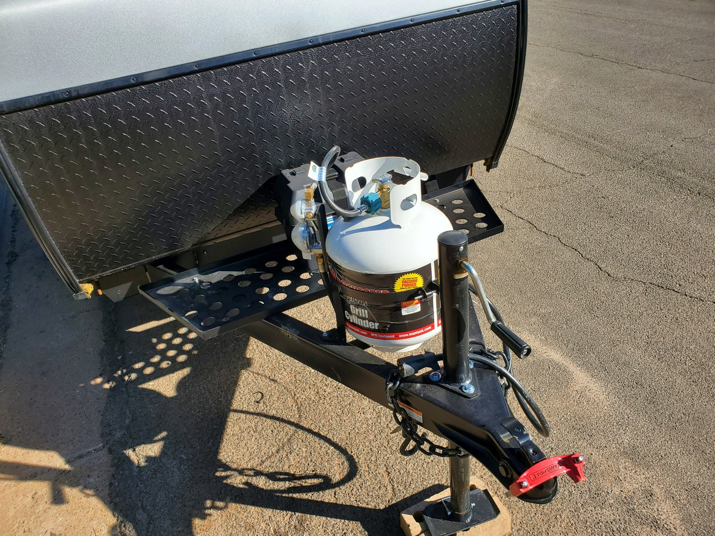 RV rental trailer's front: white propane tanks, black diamond plate, and hitch with a red lock, ready for travel.