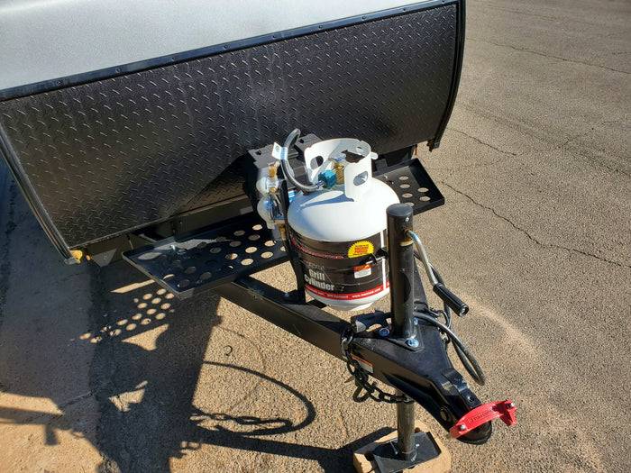 RV rental trailer's front: white propane tanks, black diamond plate, and hitch with a red lock, ready for travel.