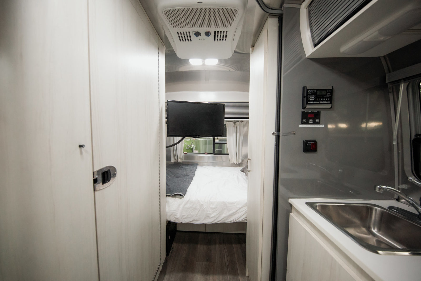 Clean rv rental interior featuring a bedroom with TV, and a kitchen area with sink and solar controls for comfortable travel.