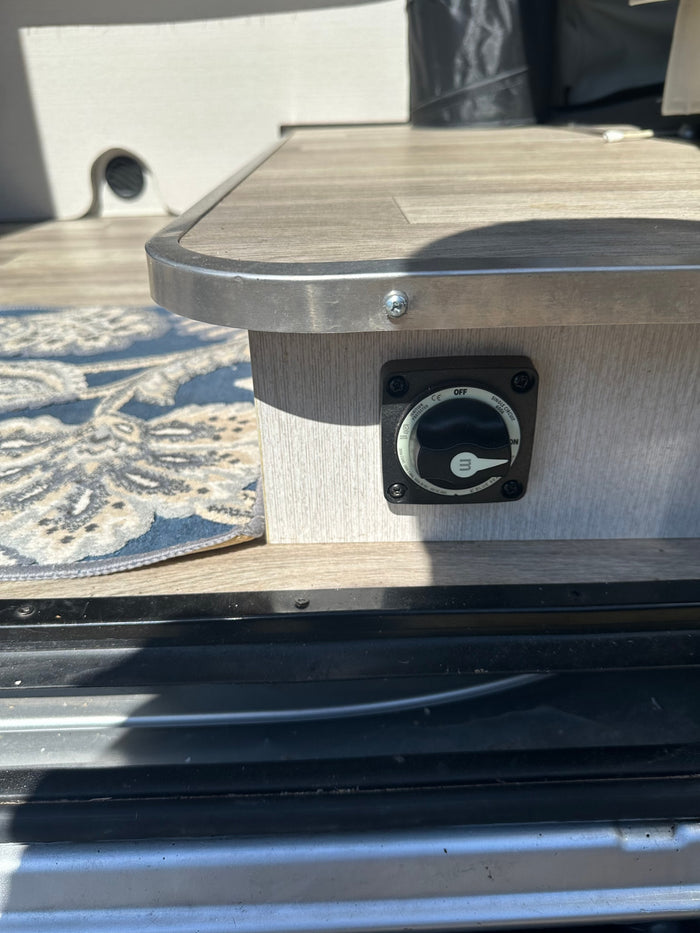 Power management on an rv rental: a Blue Sea battery switch set to 'OFF,' mounted on a wood-grain panel.