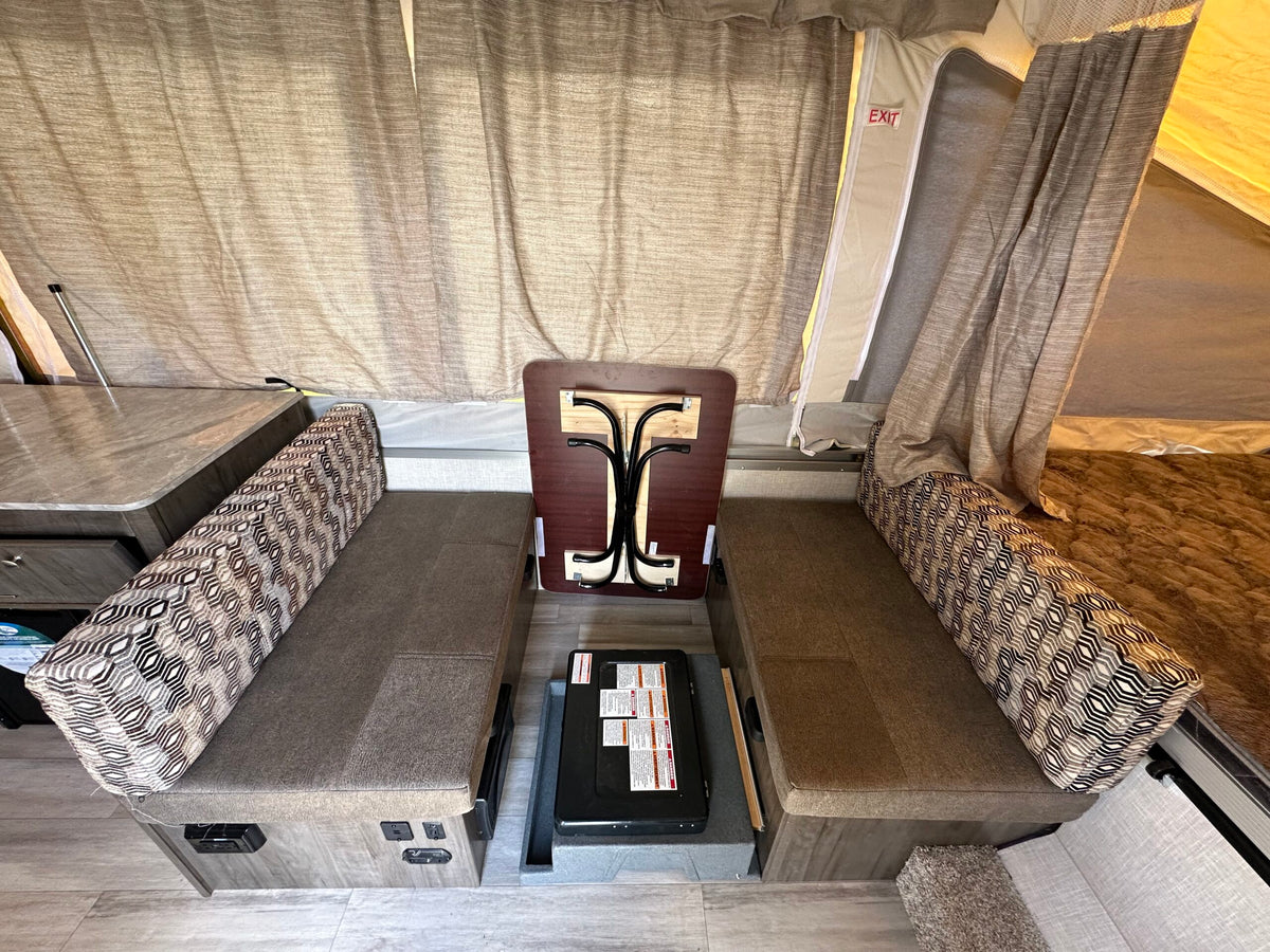 Pop-up RV rental interior: Dinette seating, a stowed table, portable stove, and tent walls with exit sign. — photo 6